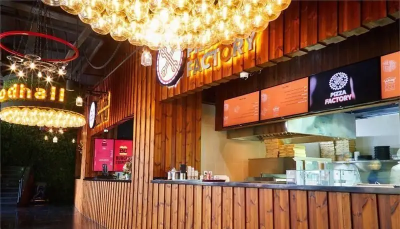 تصویری از فودکورت پلاتین فود گاردن با غرفه‌های متنوع پیتزا فکتوری و برگر. دکوراسیون چوبی و نورپردازی مدرن فضای جذابی ایجاد کرده است.
