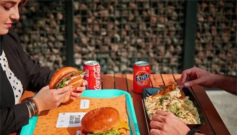 میهمانی لذت‌بخش در پلاتین فود گاردن: مشتریان در حال لذت بردن از همبرگرهای آبدار، پاستای خامه‌ای و نوشیدنی‌های خنک در فضای باز و دلپذیر.