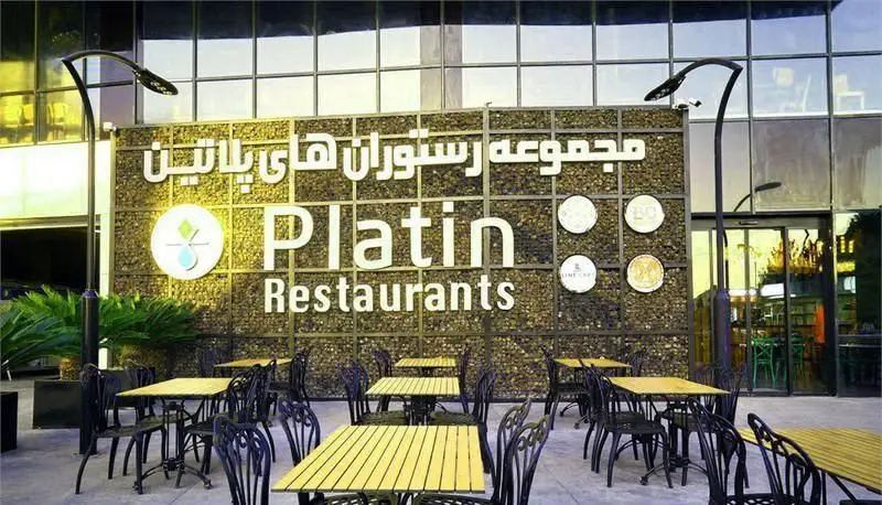 نمای بیرونی رستوران پلاتین فود گاردن با فضای غذاخوری روباز. میز و صندلی‌های فلزی و چوبی، همراه با تابلوی "Platin Restaurants" در زمینه سنگی.