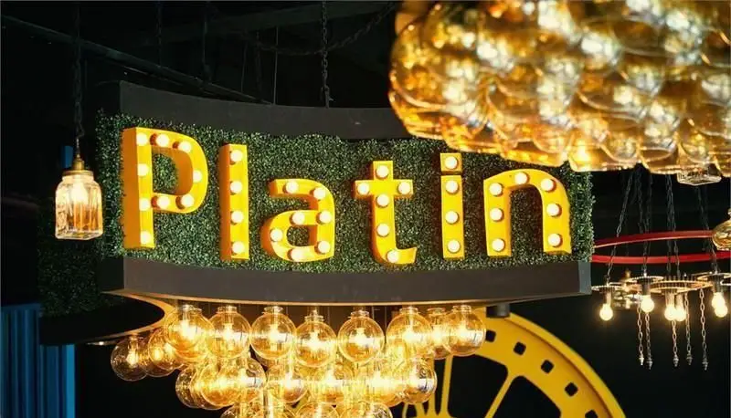تابلو بزرگ نورانی "پلاتین فود گاردن" با حروف زرد درخشان روی پس‌زمینه سبز، همراه با لوسترهای طلایی و طراحی داخلی مدرن.
