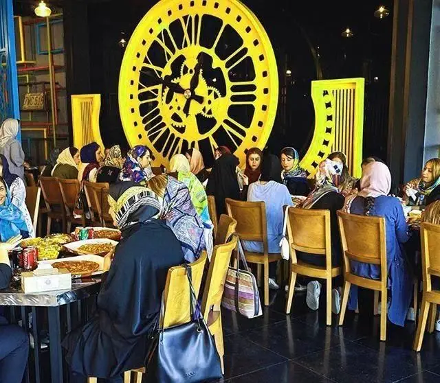 تصویری از پلاتین فود گاردن: مشتریان زن در حال لذت بردن از غذا در فضایی با دکوراسیون جذاب شامل ساعت بزرگ زرد رنگ.