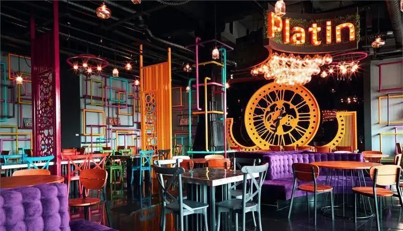 نمایی از دکوراسیون داخلی خاص و هنری پلاتین فود گاردن با مبلمان بنفش، میز و صندلی‌های رنگارنگ و ساعت‌های بزرگ.