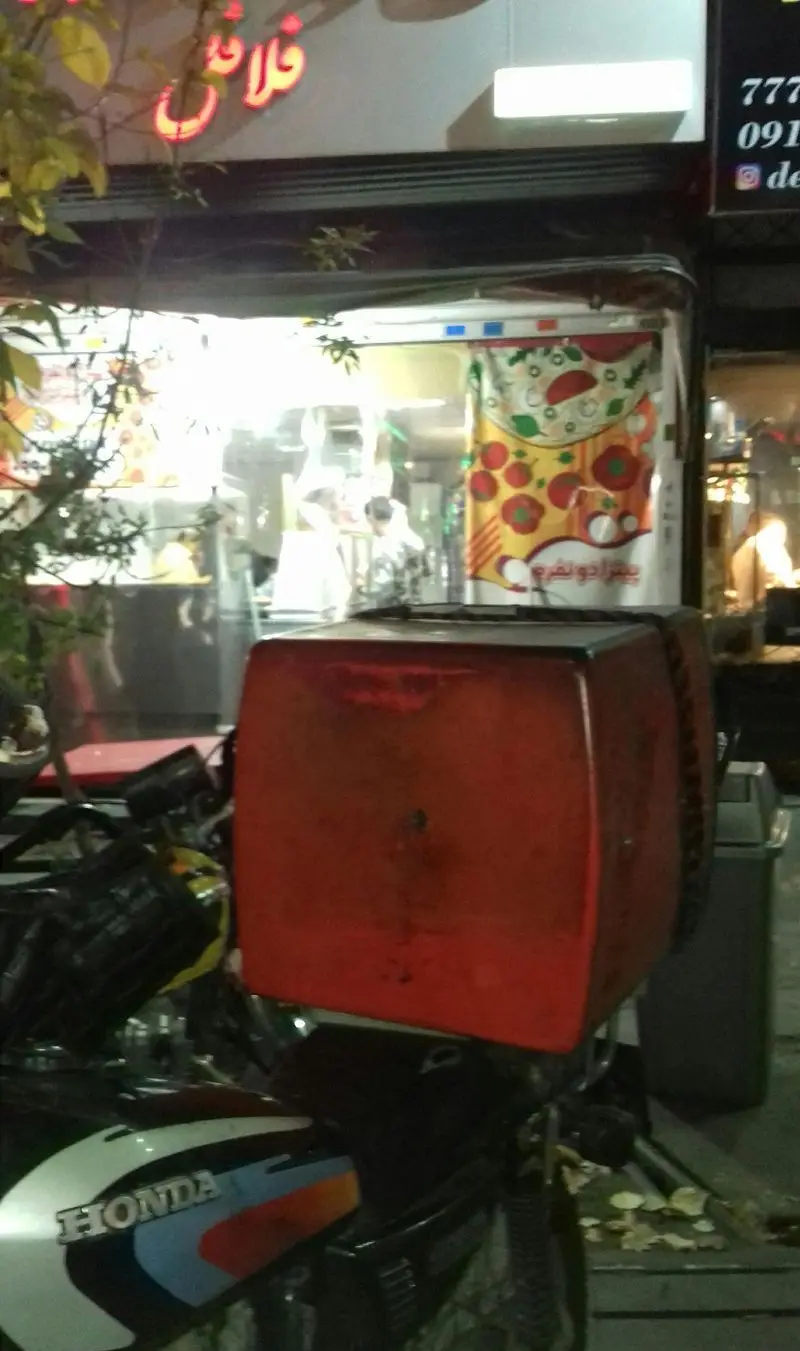 نمای شبانه از فست فود و پیتزا خان‌ دایی با موتورسیکلت هوندا مجهز به باکس دلیوری قرمز، آماده ارسال سفارشات پیتزا.