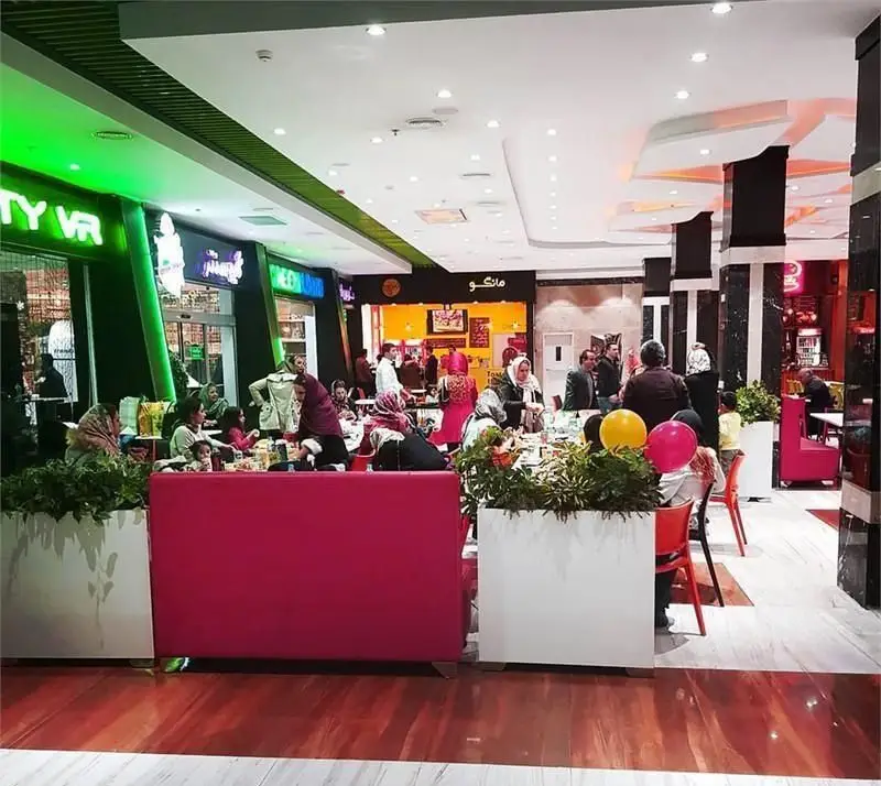 نمای داخلی پرجنب‌وجوش پیتزایی مانگو در فودکورت، مشتریان و خانواده‌ها در حال صرف پیتزا و غذاهای دیگر در محیطی مدرن و دلپذیر.