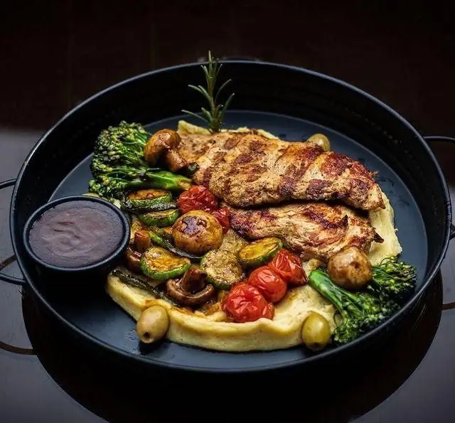 تجربه طعم خوشمزه مرغ گریل در کافه رستوران کاسا دل شف با سبزیجات کبابی (بروکلی، قارچ و گوجه گیلاسی)، پوره سیب زمینی و سس مخصوص، یک غذای کامل و شیک.