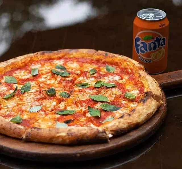 پیتزا مارگاریتا داغ و لذیذ با ریحان تازه در کافه رستوران کاسا دل شف، کنار آن یک قوطی فانتا پرتقالی سرد.