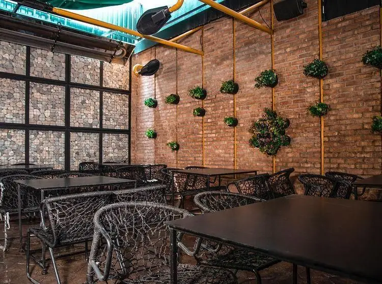 فضای داخلی کافه رستوران کاسا دل شف با دکوراسیون صنعتی و روستیک، شامل دیوارهای آجری و سنگی، میز و صندلی‌های شیک و گیاهان آویز