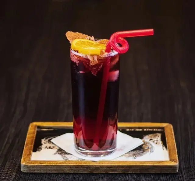 کوکتل میوه‌ای تیره و خنک کافه رستوران کاسا دل شف با برش پرتقال، نی قرمز، تزیینات جذاب و یخ روی سینی چوبی.