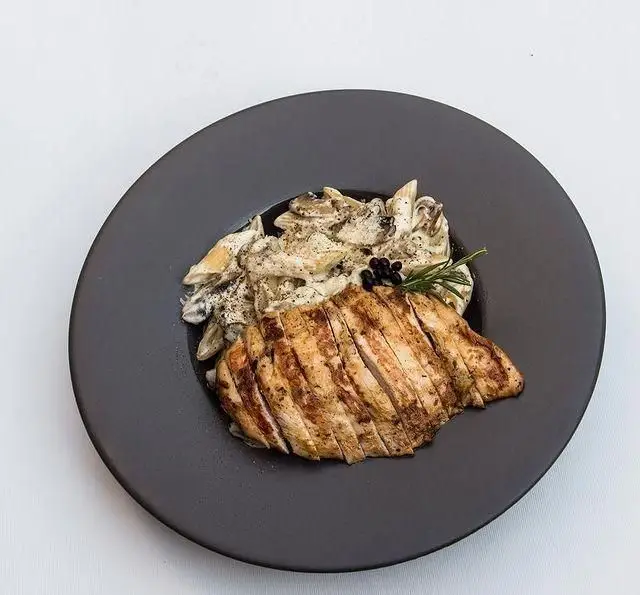 غذای لذیذ کافه رستوران کاسا دل شف: سینه مرغ گریل برش‌خورده با پاستا خامه‌ای قارچ، تزئین شده با رزماری و دانه‌های فلفل.