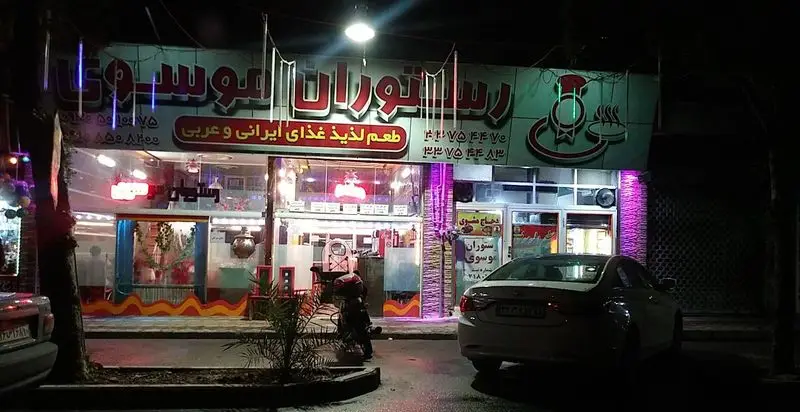 نمای شبانه رستوران موسوی با تابلوهای روشن و تاکید بر ارائه غذای لذیذ ایرانی و عربی در محیطی دلنشین
