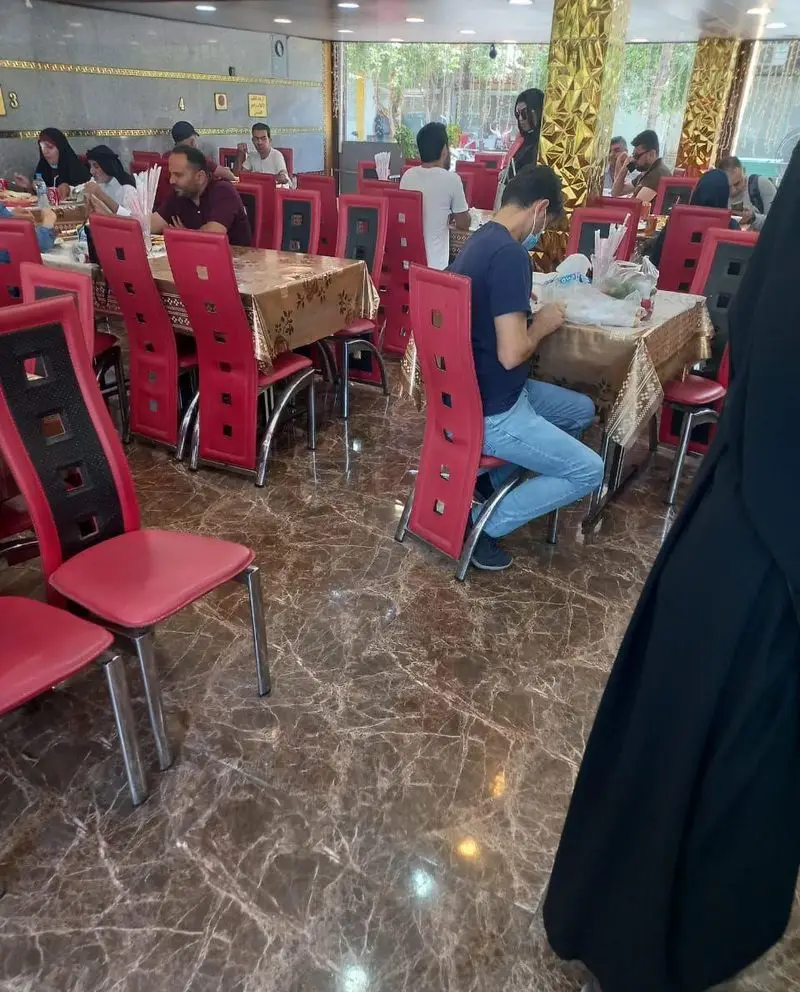 مشتریان در حال صرف ناهار یا شام در فضای داخلی دنج و مدرن رستوران موسوی با صندلی‌های قرمز، رومیزی‌های طلایی و دکوراسیون شیک.