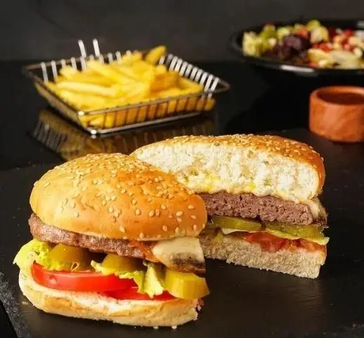 همبرگرهای لذیذ سیب ۳۶۰ با نان کنجدی، پنیر، سبزیجات تازه، سیب زمینی سرخ کرده طلایی و سالاد رنگارنگ، یک وعده کامل فست فود.