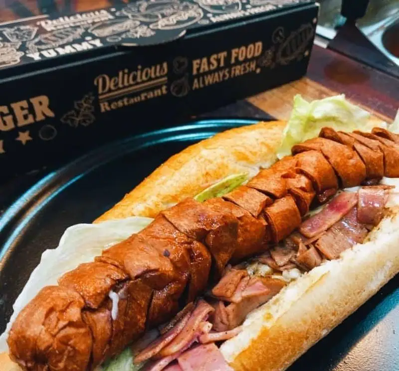 هات داگ ساندویچ سوسیس گریل شده و بیکن در نان باگت تازه، غذایی خوشمزه و پرطرفدار از سیب ۳۶۰. انتخابی عالی برای فست فود.