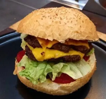 دوبل چیزبرگر خوشمزه و آبدار سیب ۳۶۰ با پنیر آب شده، کاهو تازه، گوجه و نان کنجدی، آماده برای سفارش در رستوران سیب ۳۶۰.