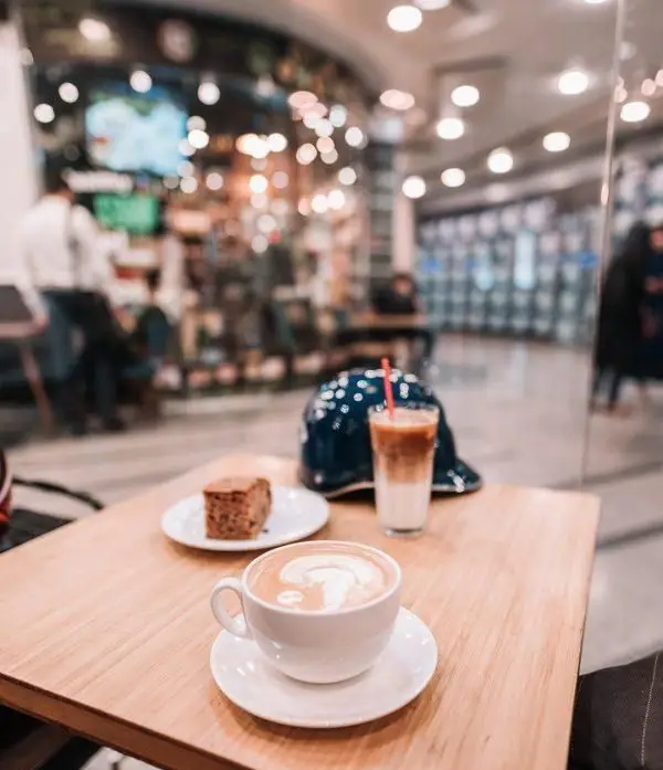 لذت نوشیدن قهوه در کافه لمیز: لاته گرم با طرح زیبا، قهوه سرد و کیک لذیذ روی میز چوبی. فضایی دلپذیر برای مشتریان.