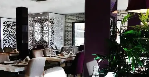 طراحی داخلی شیک و مدرن کافی شاپ تیفانی با میز و صندلی‌های چیدمان شده، پنل‌های دیواری طرح‌دار، دیوارهای آجری و گیاهان سبز.