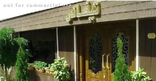 نمای بیرونی کافی شاپ تیفانی، ساختمان با روکش چوبی قهوه‌ای، درب ورودی شیک، تابلوی طلایی "تیفانی" و گلدان‌های سرسبز اطراف ورودی.