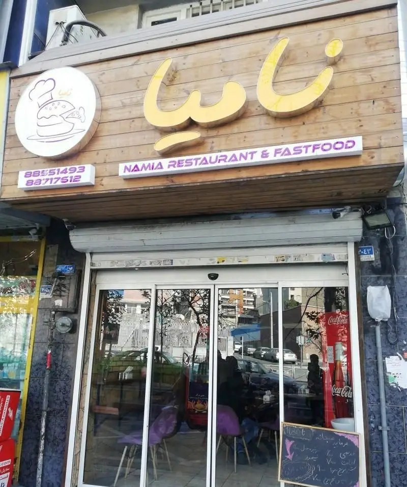 نمای بیرونی فست فود و رستوران نامیا: تابلوی چوبی، لوگوی همبرگر و پیتزا، حروف برجسته، شماره تماس و درب ورودی شیشه‌ای.