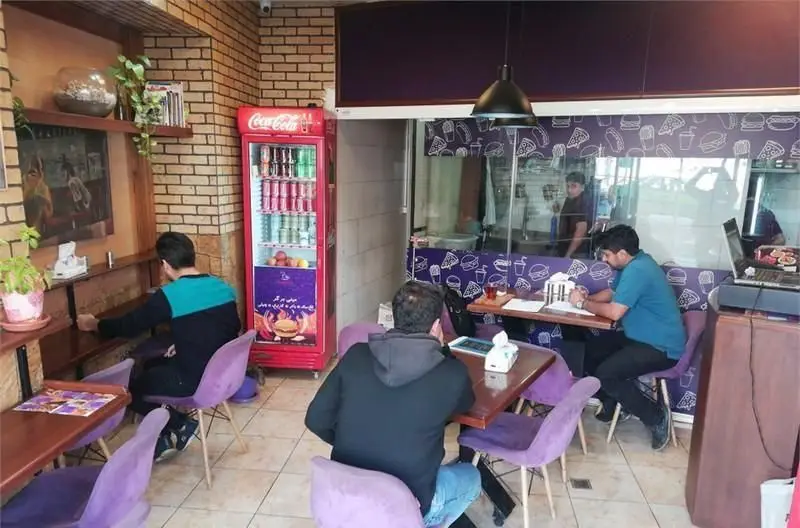 فضای داخلی شیک فست فود نامیا با مشتریان، میز و صندلی‌های بنفش، دکوراسیون دیواری جذاب، یخچال نوشیدنی و پیشخوان خدمات.