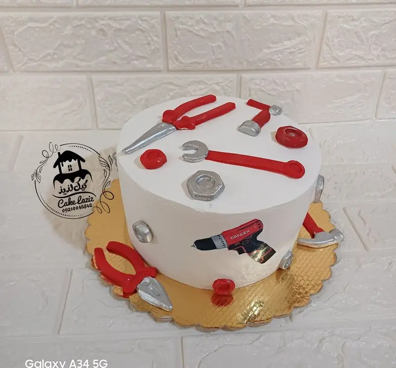 کیک تولد مردانه و پسرانه با تم ابزارآلات شامل انبردست، آچار، چکش و دریل، طراحی خاص و زیبا با رنگهای سفید و قرمز.