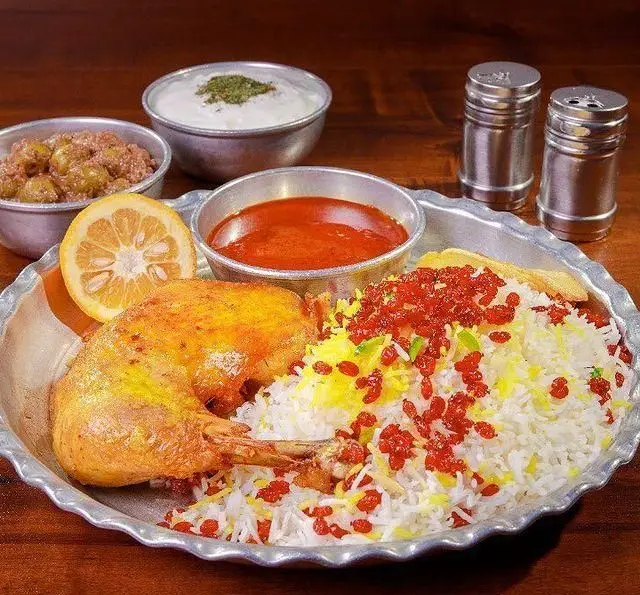 زرشک پلو با مرغ زعفرانی و زرشک فراوان، به همراه ماست و خورشت در بشقاب سنتی، از رستوران ایرانی برادران حاجی عباسی.