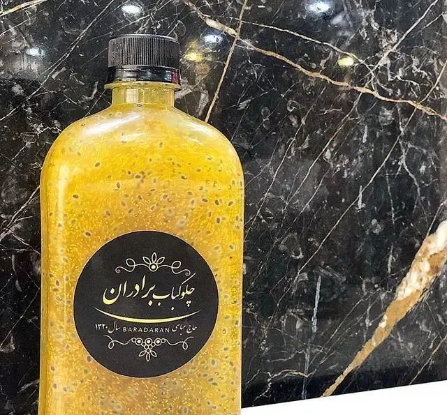 بطری نوشیدنی سنتی خنک ایرانی با تخم شربتی، محصول ویژه رستوران برادران حاجی عباسی، با پس‌زمینه مرمری سیاه.