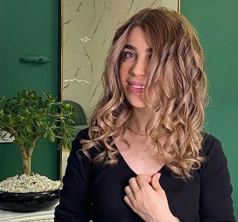 مدل موی فر درشت دخترانه با رنگ موی قهوه‌ای روشن و هایلایت‌های شیک، مناسب برای ایده استایل مو و آرایش در سالن زیبایی