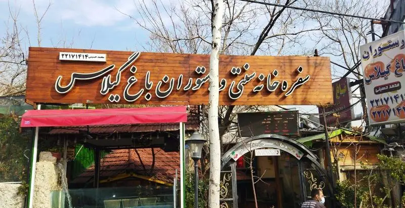تصویر نمای بیرونی رستوران و سفره خانه سنتی باغ گیلاس، با تابلوی چوبی بزرگ، شماره تماس ۲۲۱۷۱۴۱۴ و محیطی دلنشین برای غذای ایرانی.