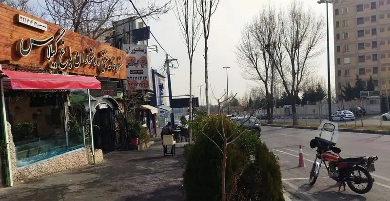 نمای بیرونی کترینگ و رستوران باغ گیلاس در روز، شامل تابلوی بزرگ، سایبان قرمز، فضای بیرونی، خیابان، درختان و ساختمانهای اطراف.