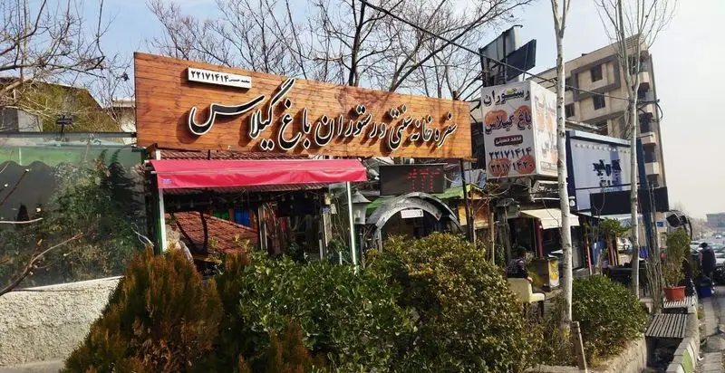 نمای بیرونی رستوران و سفره خانه سنتی باغ گیلاس با تابلوی چوبی بزرگ، سایبان قرمز و فضای سبز محیطی دلنشین را نشان می‌دهد.