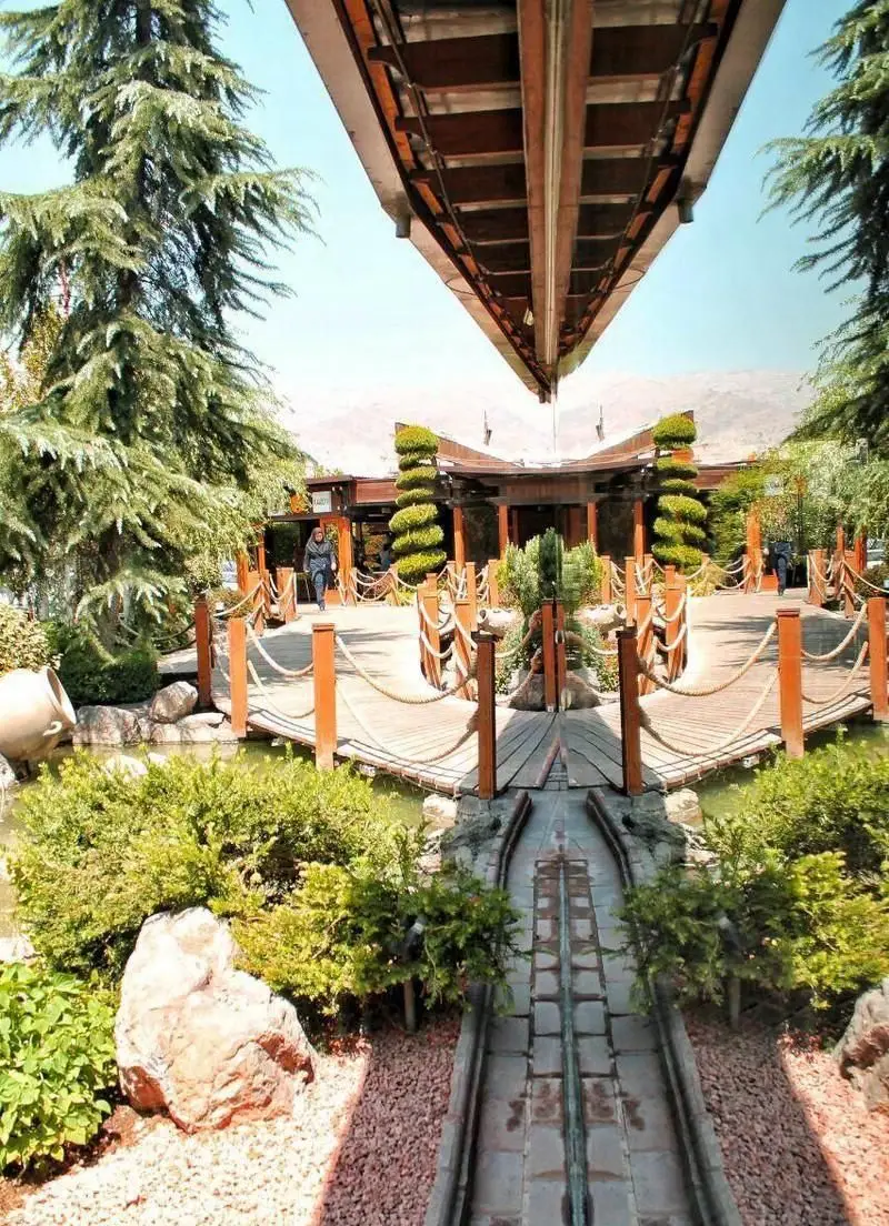 فضای سبز رستوران دنر ترد ترکیه ای با پل های چوبی، آبنما، مسیرهای دلنشین و سازه هوایی منحصر به فرد، محیطی زیبا برای مهمانان.