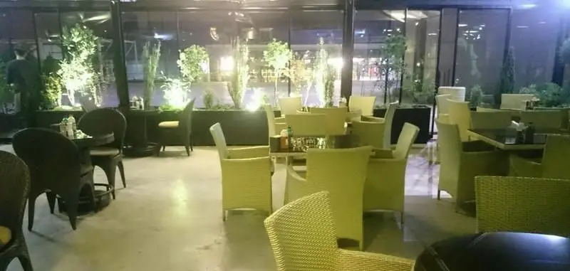 فضای دلنشین کافی شاپ ایزار با میز و صندلی‌های شیک، نورپردازی هنرمندانه و گیاهان سرسبز، محیطی ایده‌آل برای دورهمی‌های دلپذیر شبانه.