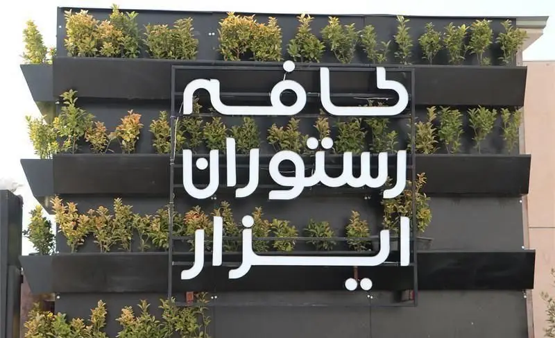 تصویری از تابلوی بزرگ کافه رستوران ایزار بر روی نمای سبز ساختمان، با گلدان‌های دیواری مدرن، معرفی کافی شاپ ایزار و خدمات.