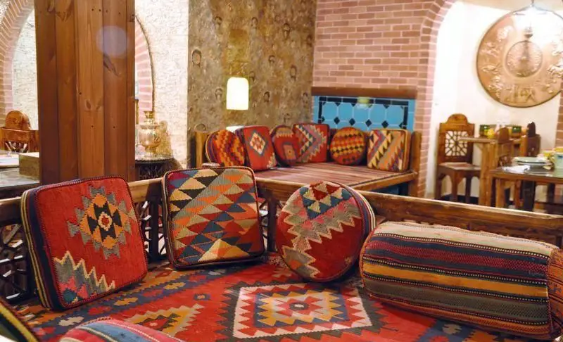 فضای داخلی سرای سنتی سیمرغ آبی با چیدمان اصیل ایرانی شامل فرش، پشتی و کوسن‌های دستباف رنگارنگ، و مبلمان چوبی زیبا.