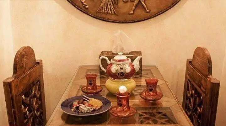 دکوراسیون سنتی سرای سنتی سیمرغ آبی با میز و صندلی چوبی، قوری چای و خوراکی‌های سنتی، فضایی اصیل و دلپذیر.