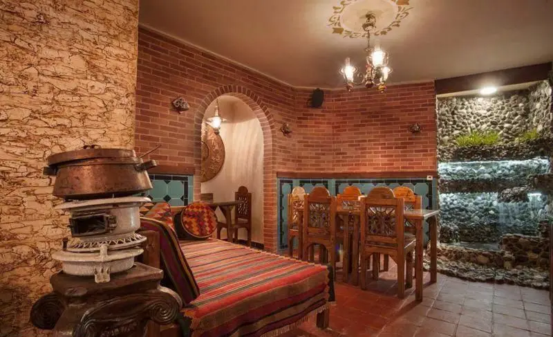 نمایی از دکوراسیون داخلی سرای سنتی سیمرغ آبی شامل دیوار آجری، تخت سنتی با تشک راه راه، میز و صندلی چوبی و حوض آب سنگی.