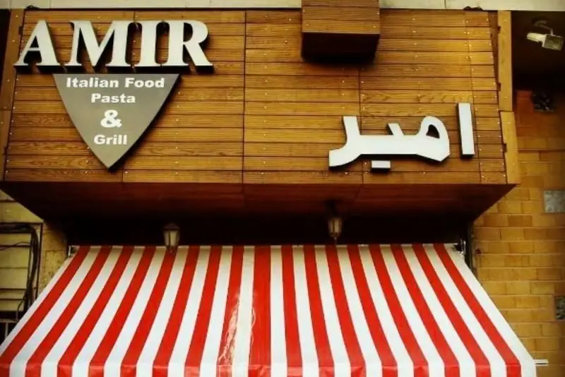 نمای بیرونی رستوران ایتالیایی امیر گریل: تابلو با پاستا، گریل و دکور چوبی، سایبان راه راه قرمز و سفید.