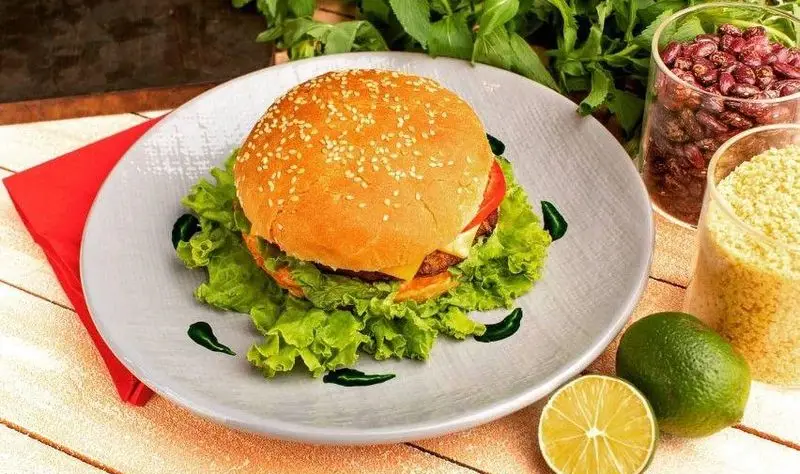 برگر لذیذ و سالم فست فود هایدا با کاهو، پنیر، گوجه و نان کنجدی، در کنار مواد اولیه تازه و لیموترش.