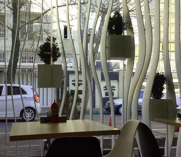 تصویری از فضای دلنشین فست فود گیو؛ نمایی از میز و صندلی‌های مدرن، دکوراسیون خاص پنجره با گیاهان سبز و منظره خیابان.