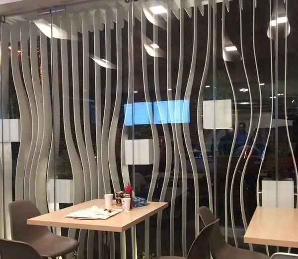 نمای داخلی فست فود گیو با دکوراسیون مدرن و پنجره‌های شیشه‌ای طرح‌دار موجی، میز و صندلی‌های قهوه‌ای برای مشتریان.