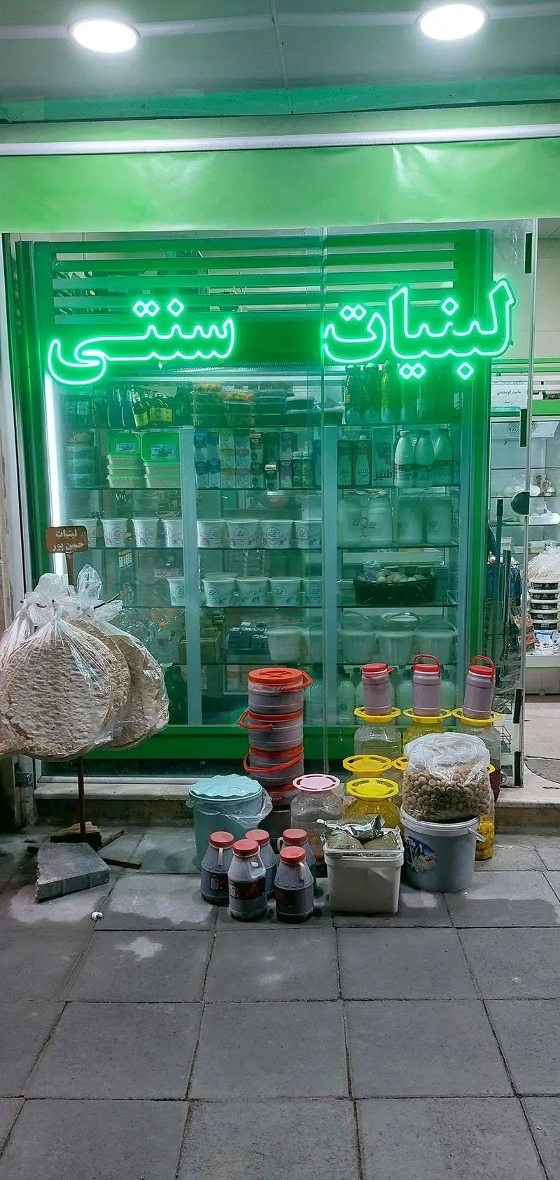 تصویر نمای بیرونی مغازه لبنیات سنتی گلبانان(هدایتی) با محصولات تازه محلی مانند دوغ، ماست، پنیر، نان و ترشیجات آماده فروش.