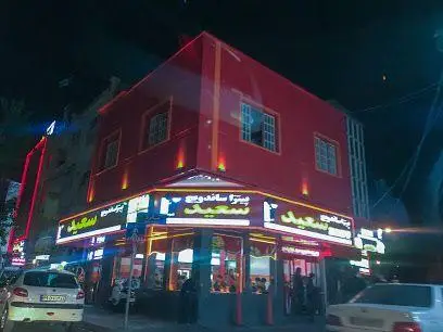 پیتزا و ساندویچ سعید، فست فودی محبوب با نورپردازی جذاب و تابلوهای درخشان در شب. این رستوران انواع غذاهای فست فود را ارائه می‌دهد.