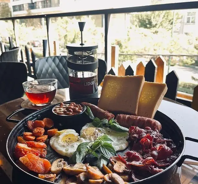 میز صبحانه کامل و لذیذ کافه رستوران فروهر با تخم مرغ، سوسیس، بیکن، لوبیا، قارچ، سبزیجات و نان تست در فضایی دلنشین.