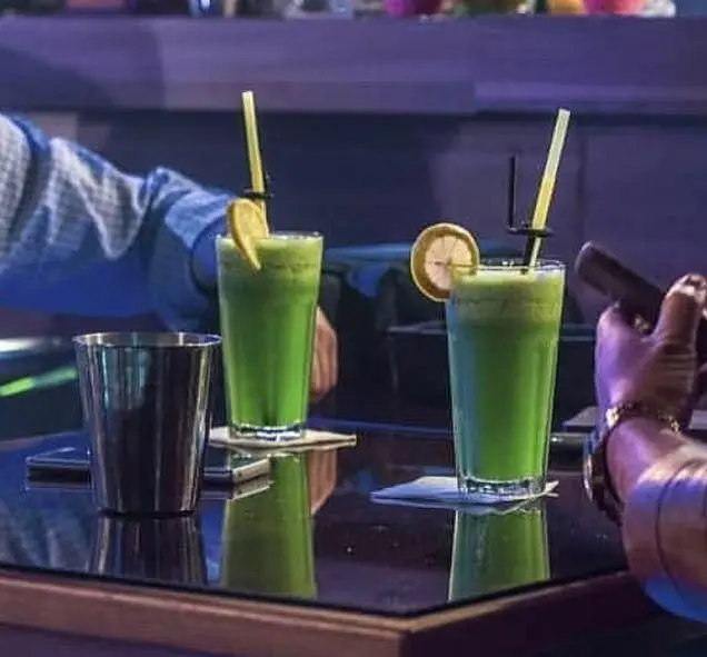 تصویری از دو لیوان نوشیدنی سبز جذاب و تازه با تزیین لیمو و نی روی میز شیشه‌ای در کافه رستوران فروهر، فضایی آرام و دلپذیر برای مشتریان.