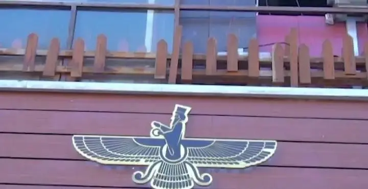 کافه رستوران فروهر: نماد فروهر طلایی درخشان بر روی نمای چوبی قهوه‌ای مایل به قرمز با حصار چوبی و پنجره‌ها در بالا.