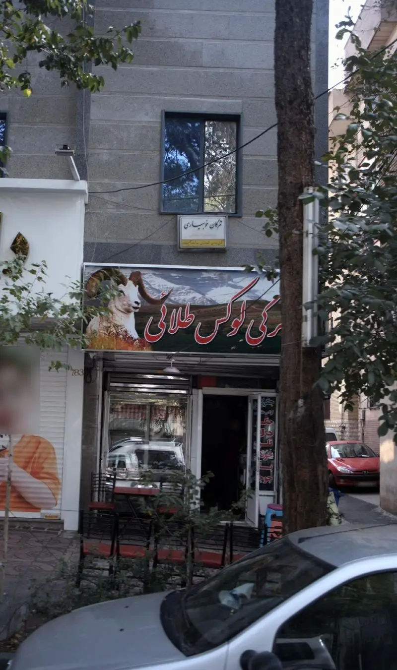 نمای بیرونی جگرکی لوکس طلائی، با تابلوی چشم‌نواز شامل گوسفند شاخ‌دار و کوهستان، میز و صندلی در پیاده‌رو، مکانی دلپذیر برای کباب.