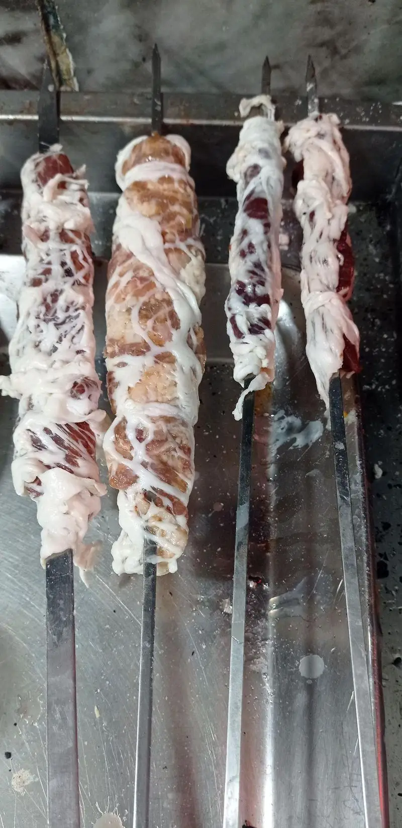 سیخ‌های جگر، دل، قلوه و گوشت گوسفندی پیچیده شده در چربی دنبه، آماده طبخ در جگرکی لوکس طلائی. کباب سنتی و خوشمزه.