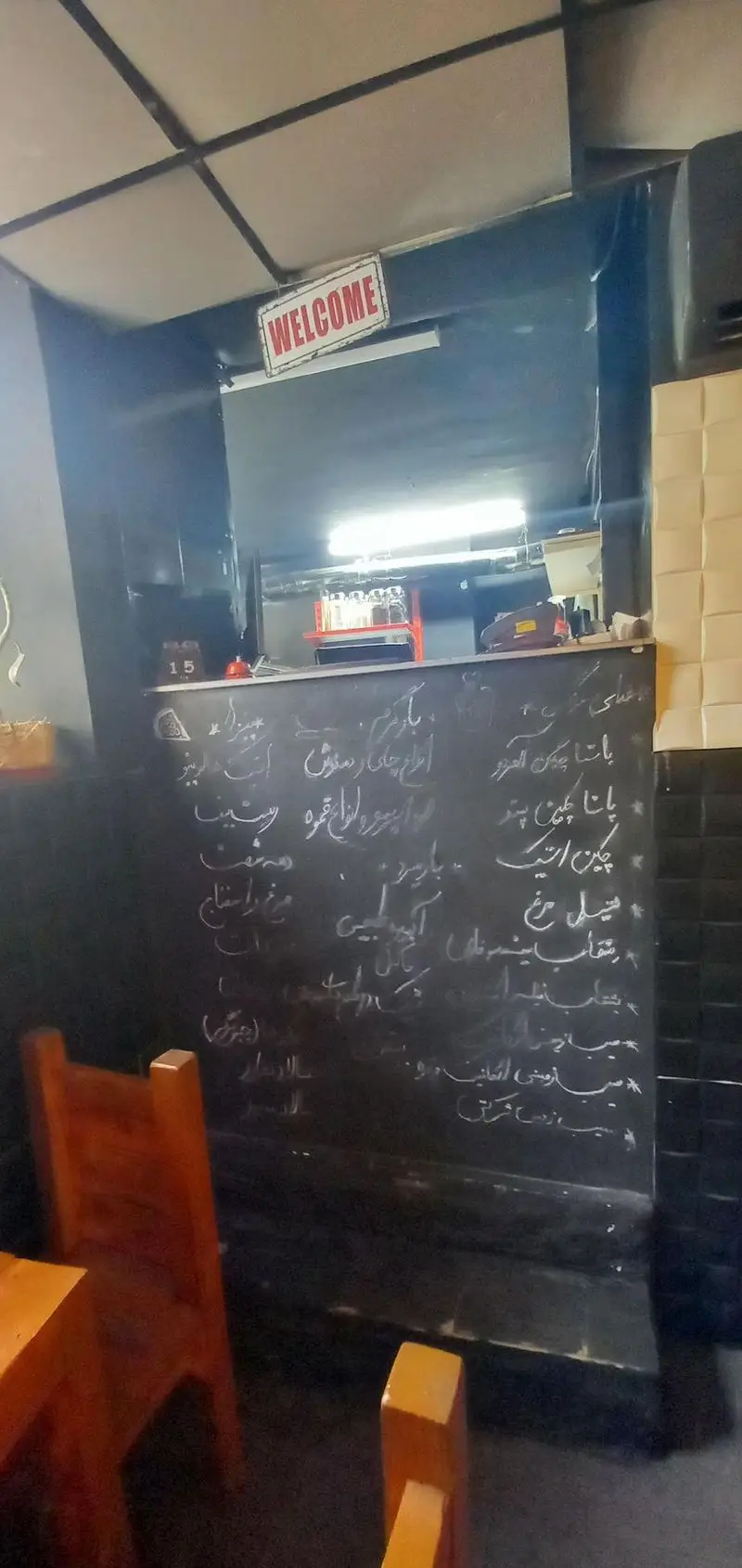 تصویری از فضای داخلی رستوران و کافه هتل آپادانا با منوی دستنویس گچی، میز و صندلی‌های چوبی. ایده‌آل برای یک تجربه غذایی دلپذیر.