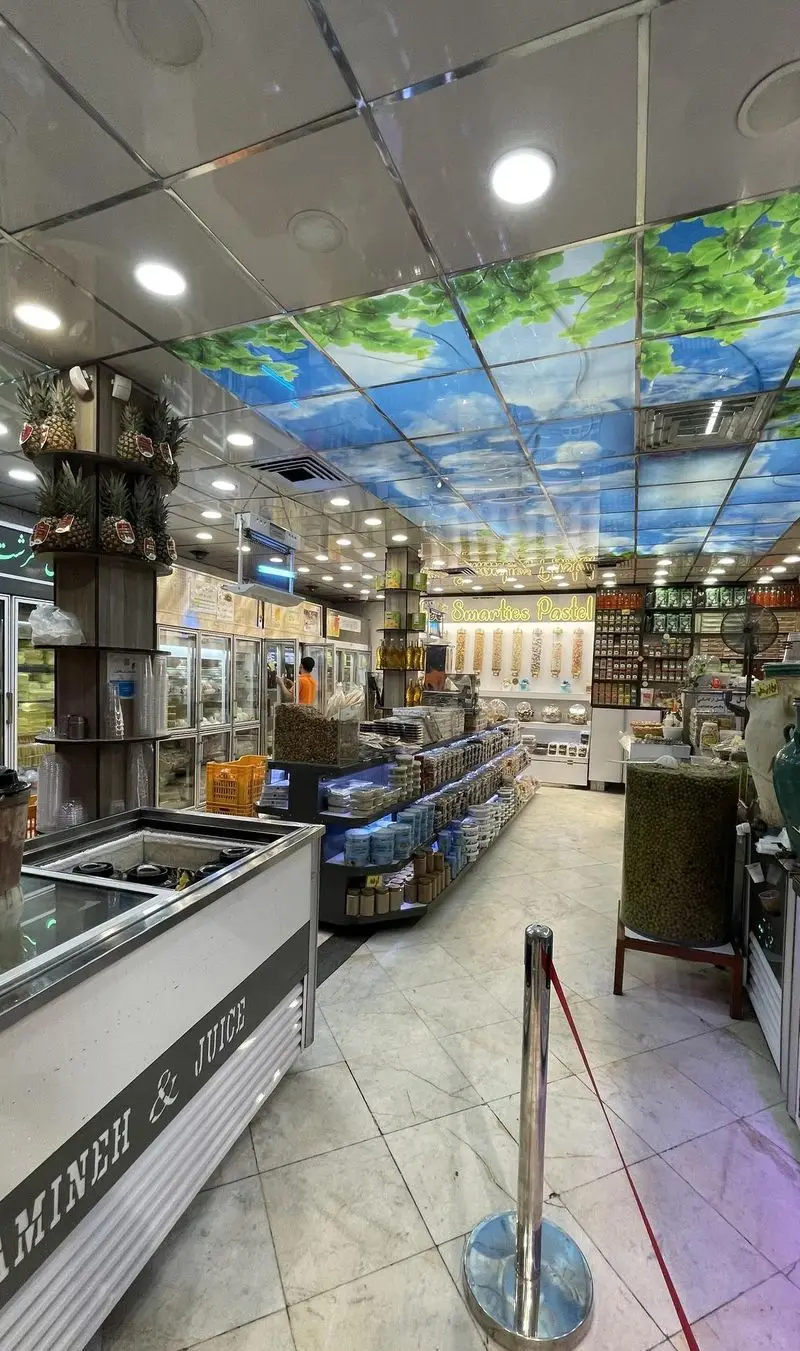 نمای داخلی فروشگاه لبنیات سنتی و آبمیوه بستنی طرشت؛ شامل قفسه‌های متنوع، یخچال‌ها، آجیل، زیتون و سقف آبی آسمانی.