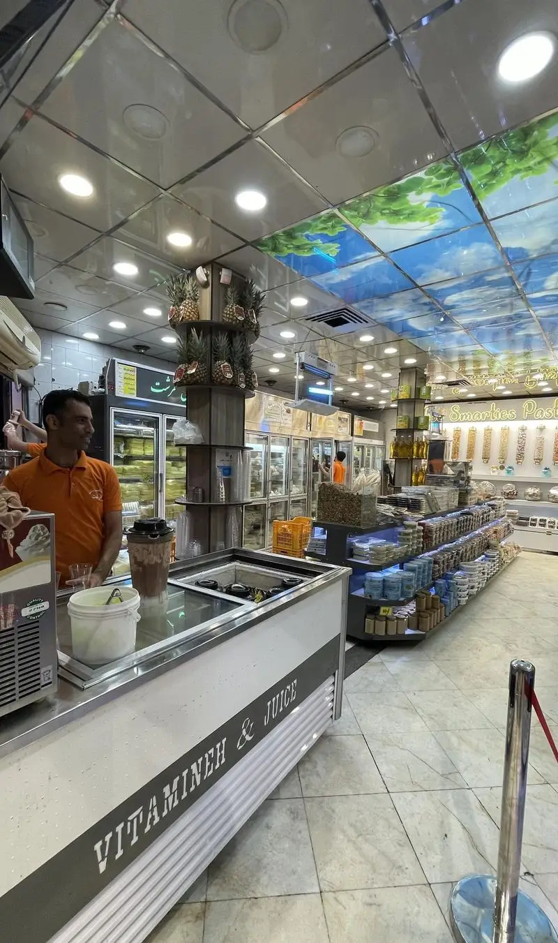 تصویر داخلی مغازه لبنیات سنتی و آبمیوه بستنی طرشت، مردی پشت پیشخوان ویتامینه و آبمیوه، با نمایش آجیل، دسر و میوه تازه.